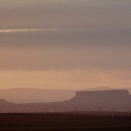 Tobiasz Brakoniecki - Silhouetted mesas and mountains fade into the distance under a hazy, peach-colored sky, with a row of power line towers sparsely dotting the foreground.