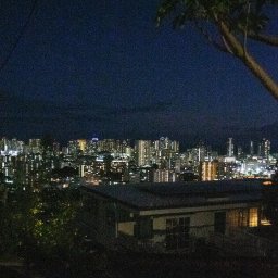 Tobiasz Brakoniecki - Nocny widok na panoramę miasta zza domu i drzewa, z widocznymi światłami budynków.