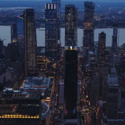 Nocny widok z góry na drapacze chmur w Nowym Jorku, z rzeką w tle i ulicami oświetlonymi światłami samochodów.