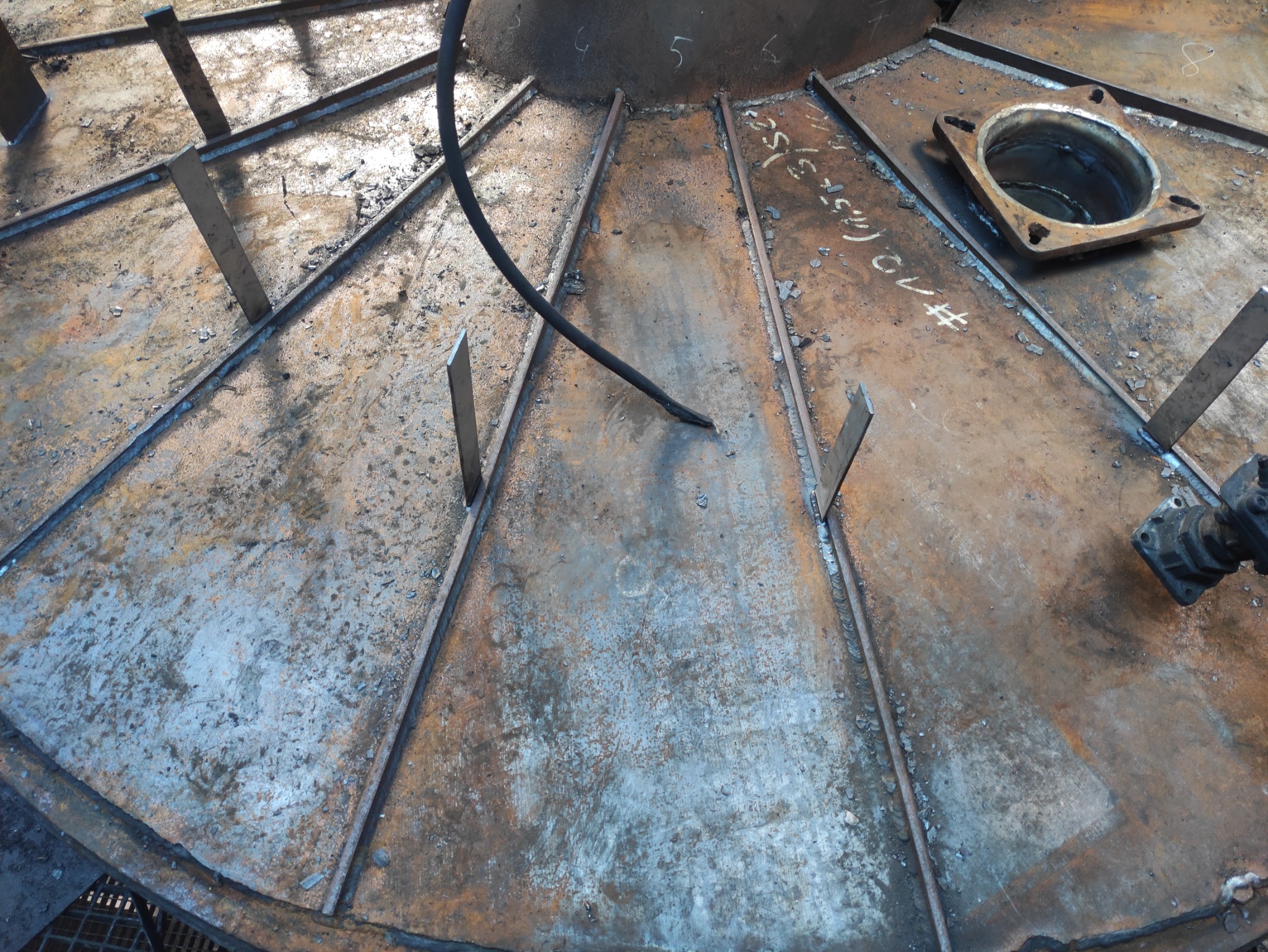 Wnętrze metalowej konstrukcji w trakcie spawania, widoczne spawy, elementy wzmacniające i otwór z kołnierzem, całość w surowym stanie.