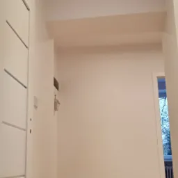 Świeżo pomalowane wnętrze mieszkania w kamienicy z parkietem w jodełkę, widoczne drzwi z nowoczesnym frezowaniem i zamontowany klimatyzator.