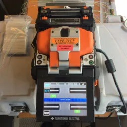 Zgrzewarka światłowodowa Sumitomo Electric TYPE-71C+ w trakcie procesu zgrzewania, widoczne włókna światłowodowe i ekran z parametrami ustawień.