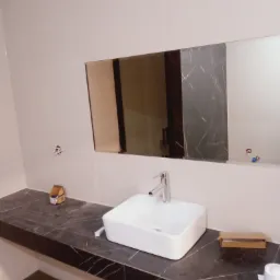 Nowoczesna łazienka z umywalką nablatową i blatem z czarnego marmuru. Widoczne białe płytki i lustro. Umywalka ma chromowaną baterię. Elementy instalacji czekają na podłączenie.