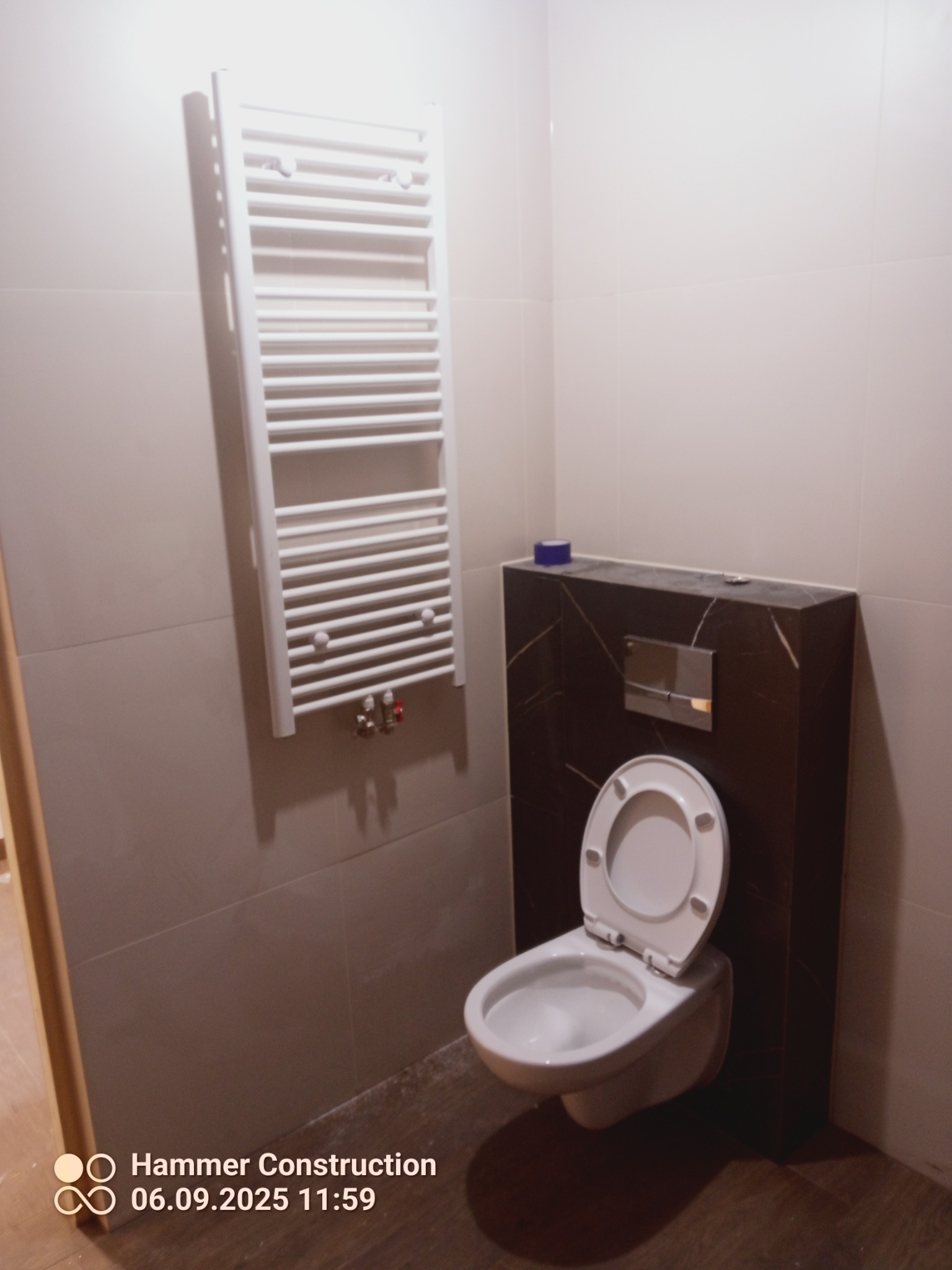 Wykończona łazienka w Smogorzowie: podwieszana toaleta z brązową obudową i grzejnik drabinkowy na beżowych płytkach. Nowoczesny design.