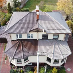 Widok z góry na dom z dachem podzielonym na dwie części: jedna strona z ciemnobrązową, świeżo pomalowaną dachówką, druga strona z szarą, prawdopodobnie umytą dachówką, ukazując efekt przed i po...