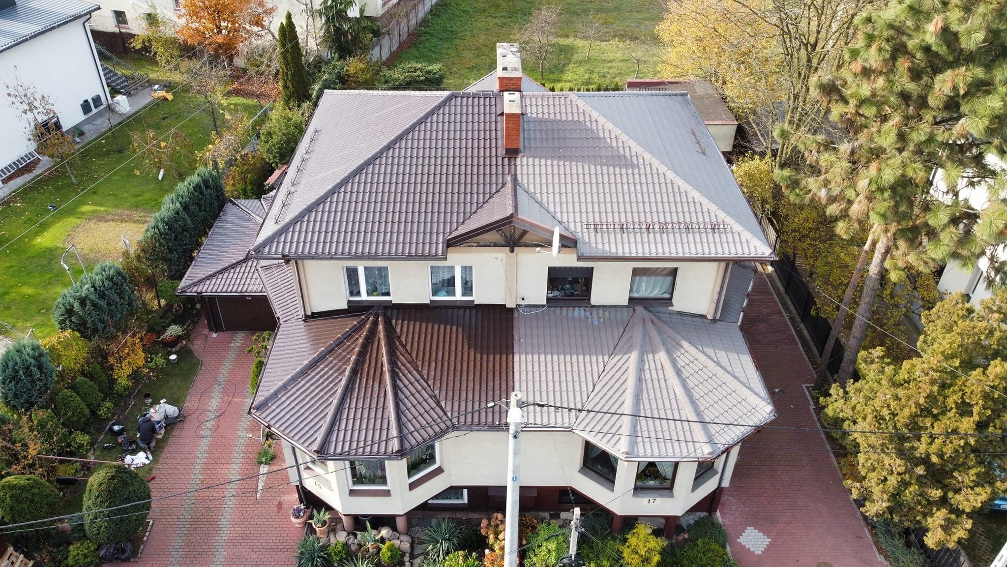 Widok z góry na dom z dachem podzielonym na dwie części: jedna strona z ciemnobrązową, świeżo pomalowaną dachówką, druga strona z szarą, prawdopodobnie umytą dachówką, ukazując efekt przed i po...