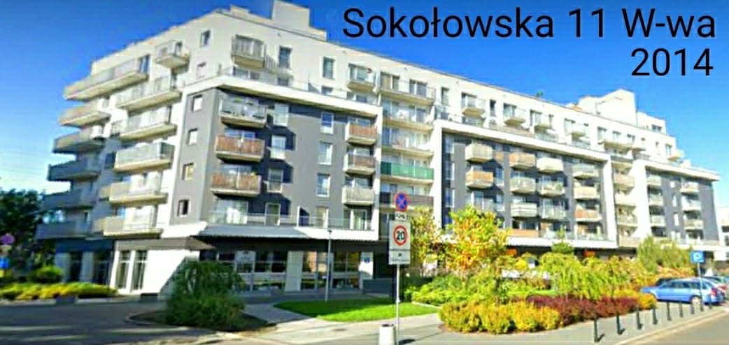 Wielopiętrowy budynek mieszkalny z balkonami, widok z poziomu ulicy, znak drogowy ograniczenia prędkości.