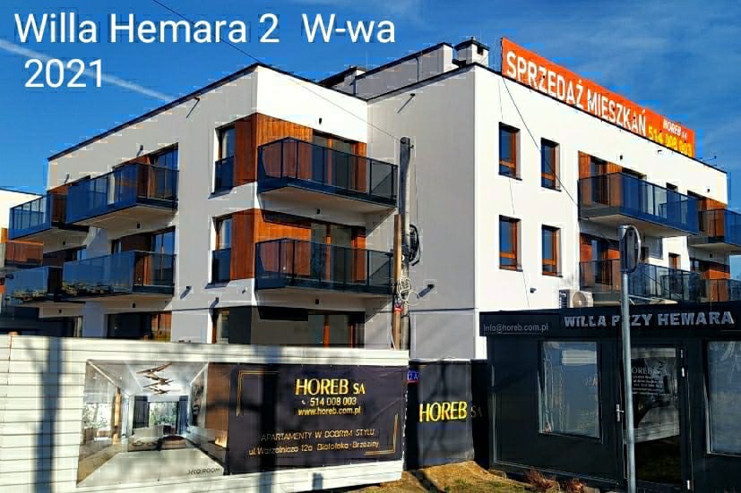 Nowoczesny budynek apartamentowy 'Willa Hemara 2' z balkonami z przezroczystymi balustradami, z widoczną reklamą sprzedaży mieszkań na dachu i banerami reklamowymi firmy deweloperskiej Horeb SA...