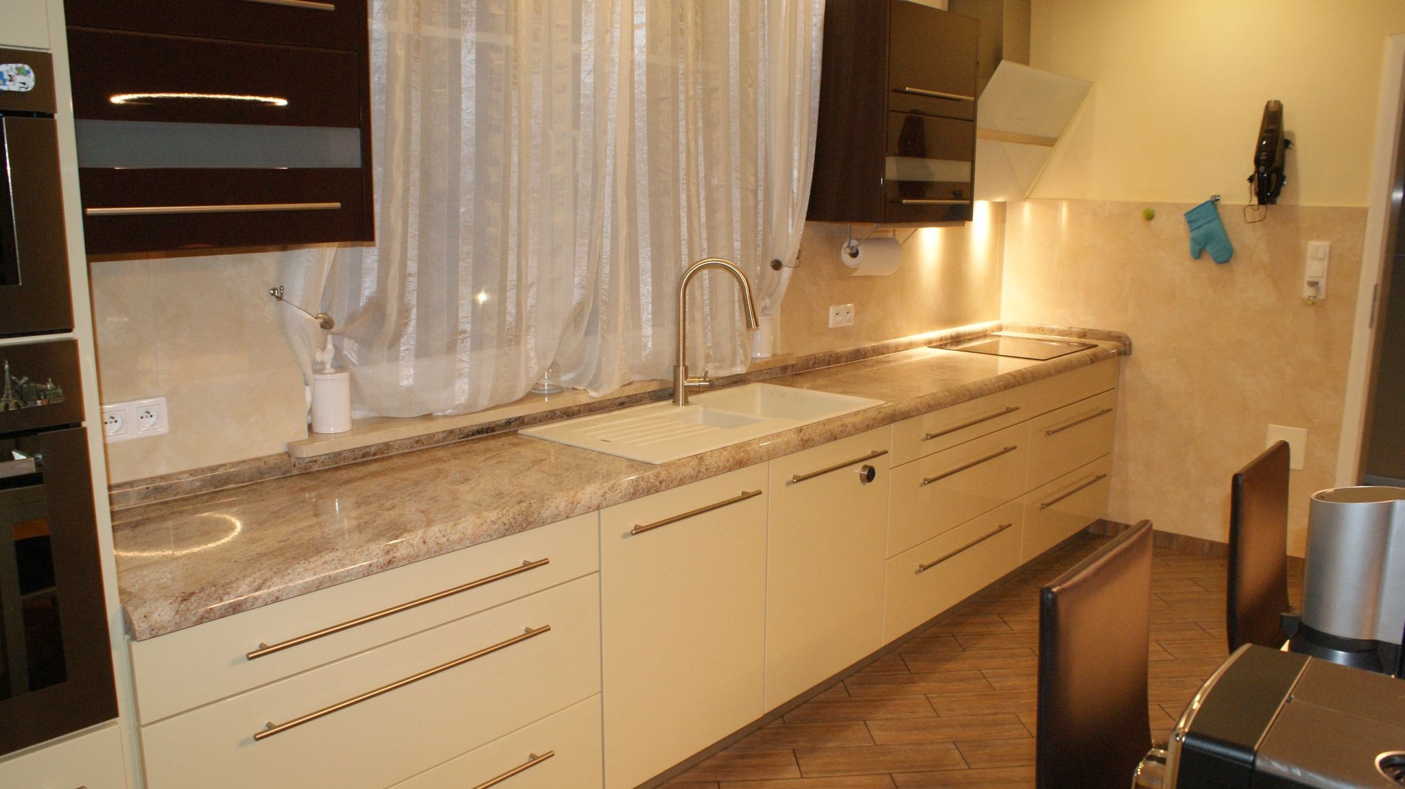 Beżowy blat kuchenny z konglomeratu w Jeleniej Górze, z wbudowanym zlewozmywakiem i baterią, widok na fragment zabudowy kuchennej z drewnianymi frontami i beżowymi ścianami.