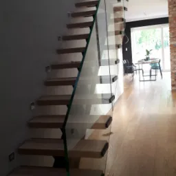 Schody drewniane z szklaną balustradą w nowoczesnym domu w Poznaniu, widok z dołu, minimalistyczny design.