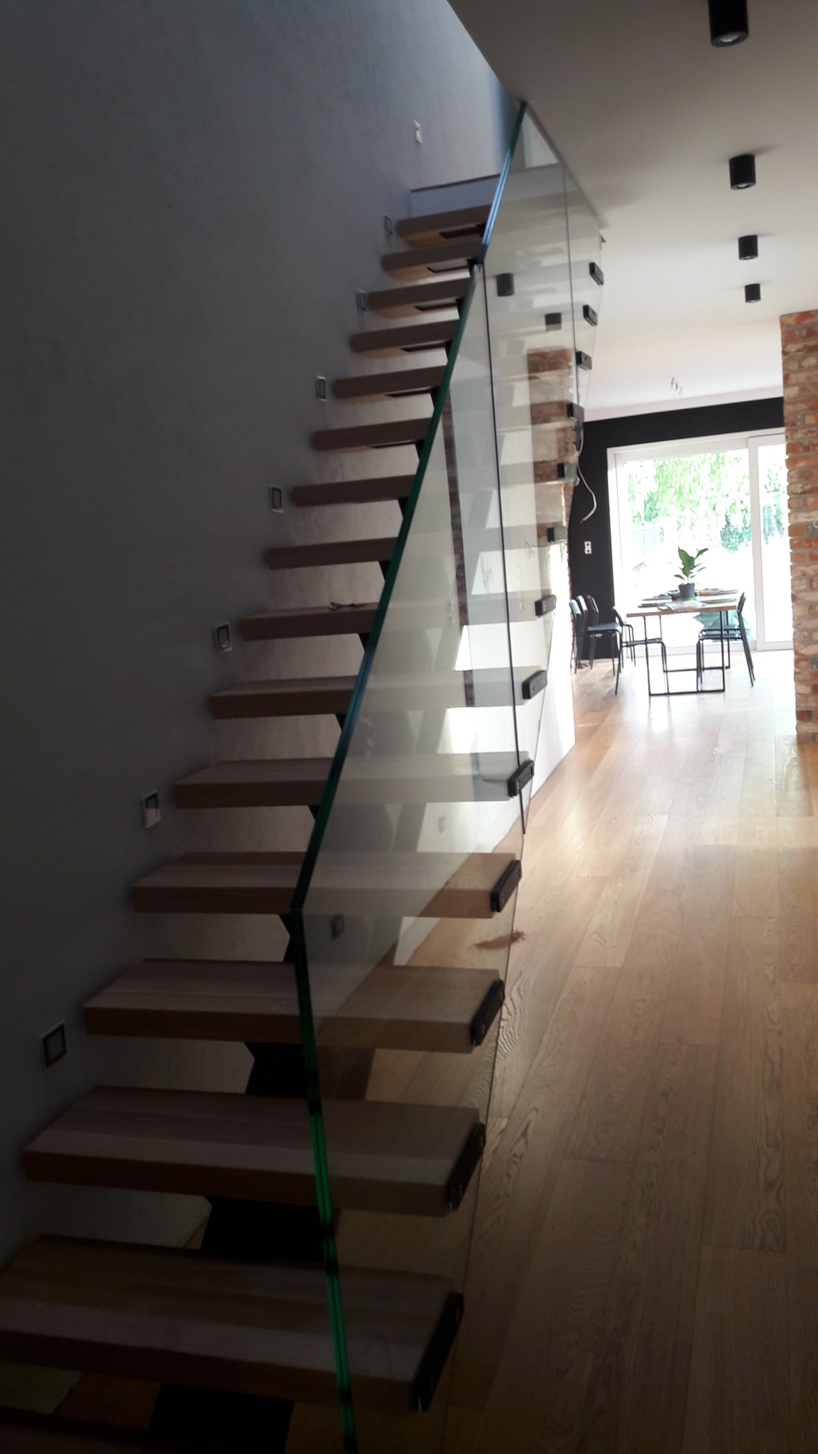 Schody drewniane z szklaną balustradą w nowoczesnym domu w Poznaniu, widok z dołu, minimalistyczny design.