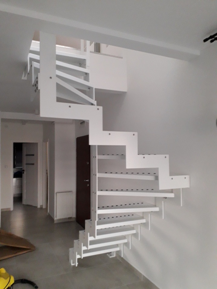 Białe, nowoczesne schody metalowe spiralne, z ażurowymi stopniami, zamontowane w jasnym wnętrzu domu.