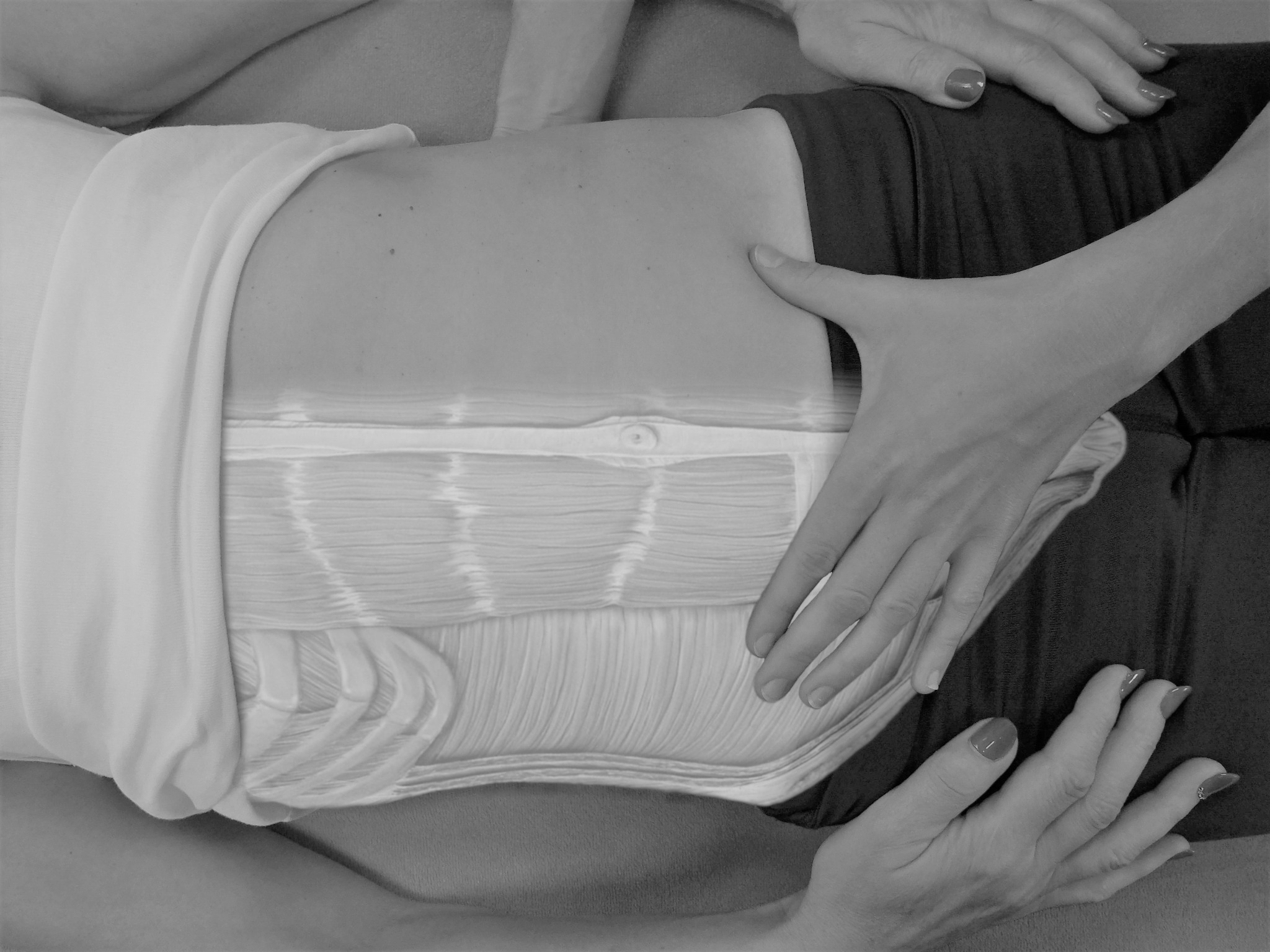 Czarno-białe zdjęcie przedstawia brzuch pacjenta poddawany terapii manualnej. Widoczne dłonie terapeuty uciskają i masują okolice mięśni brzucha, z nałożoną grafiką ilustrującą warstwy mięśniowe.