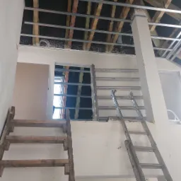 Konstrukcja metalowa podwieszanego sufitu zamontowana do drewnianej więźby dachowej, widoczne drabiny i fragmenty ścian w trakcie prac wykończeniowych.