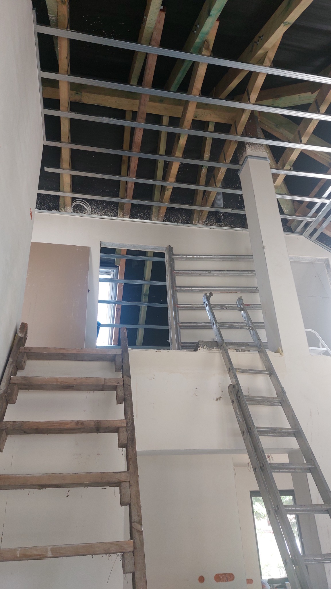 Konstrukcja metalowa podwieszanego sufitu zamontowana do drewnianej więźby dachowej, widoczne drabiny i fragmenty ścian w trakcie prac wykończeniowych.