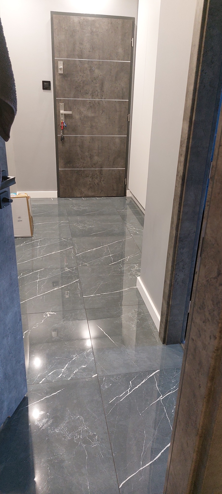 Wykończone wnętrze: szare płytki podłogowe imitujące marmur w korytarzu z szarą, nowoczesną, metalową futryną drzwi wejściowych.