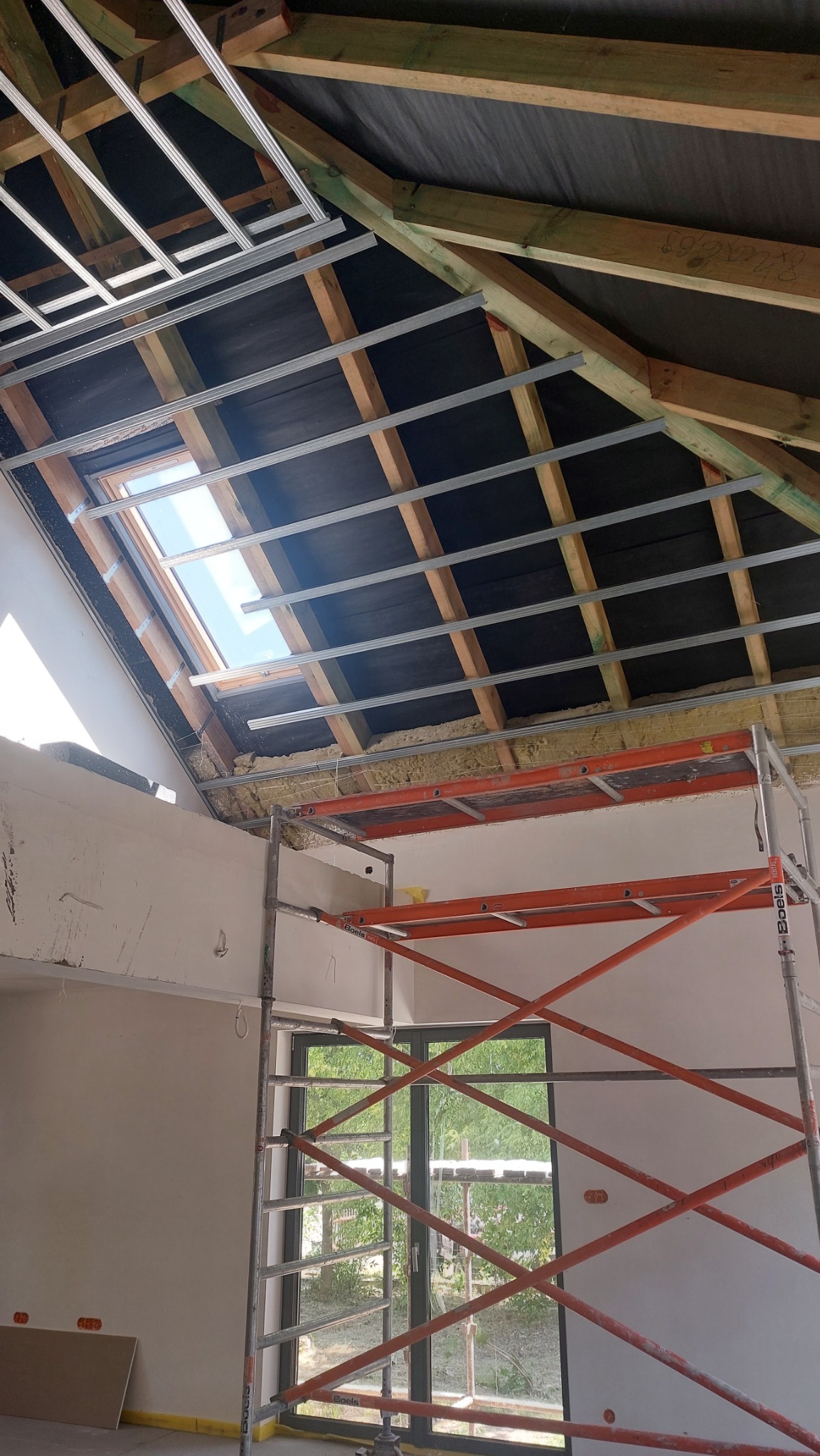 Montaż stelaża pod płytę karton gips na poddaszu, widoczne ocieplenie wełną mineralną, okno dachowe i rusztowanie.