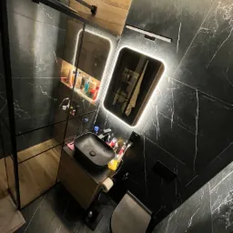 Nowoczesna łazienka z czarnymi marmurowymi płytkami, podświetlanym lustrem i kabiną prysznicową typu walk-in, widok z g&oacute;ry.