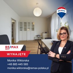 BLUETREE MONIKA WIKTORSKA - Kobieta w garniturze na tle jasnego salonu z białymi meblami, oświetlonego kulistą lampą, z logo RE/MAX w rogu i napisem 'Wynajęte'.