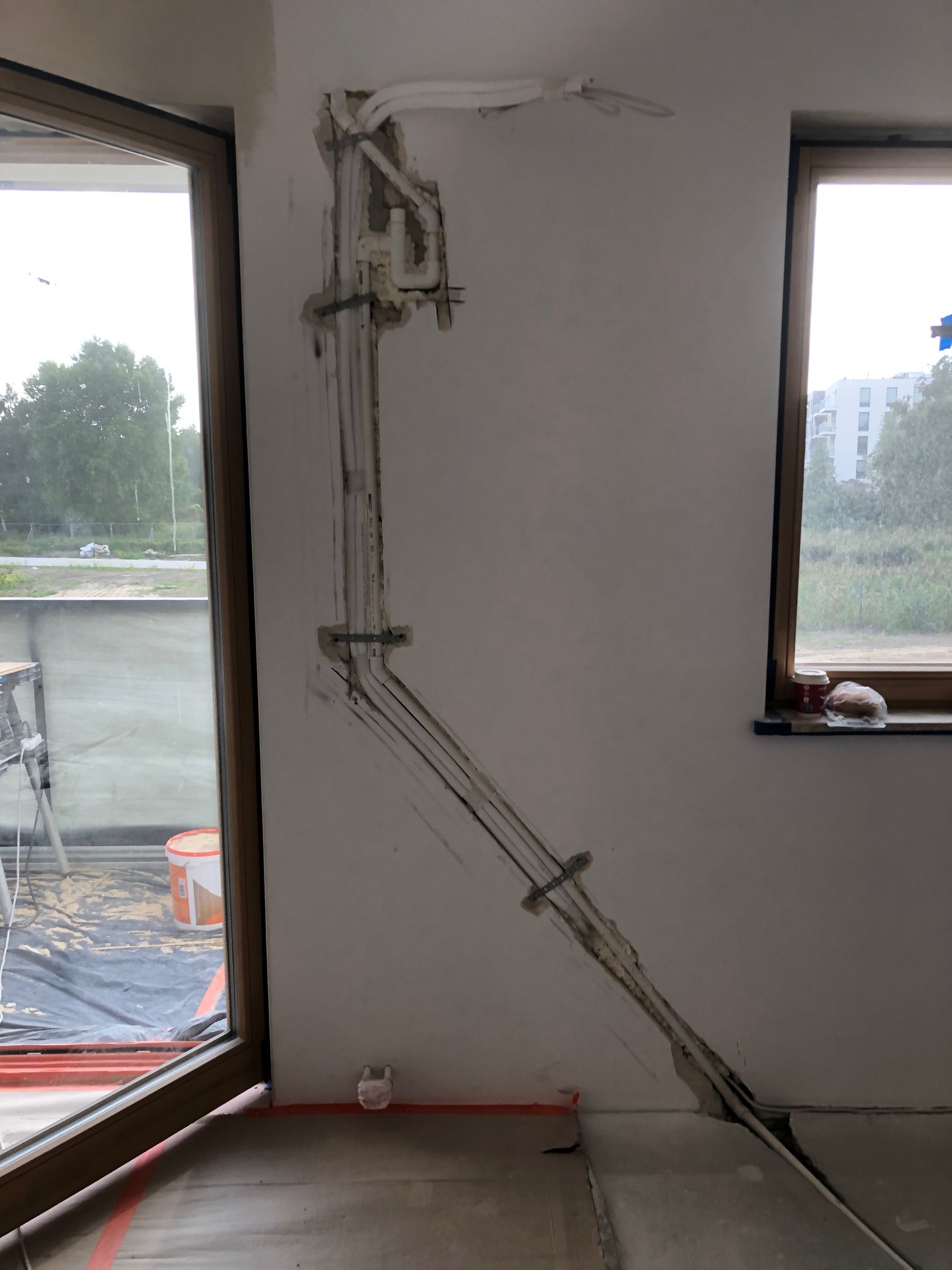 Montaż instalacji chłodniczej wewnątrz ściany w domu jednorodzinnym, widoczne rury i przewody w bruzdach, przygotowane do zakrycia tynkiem.