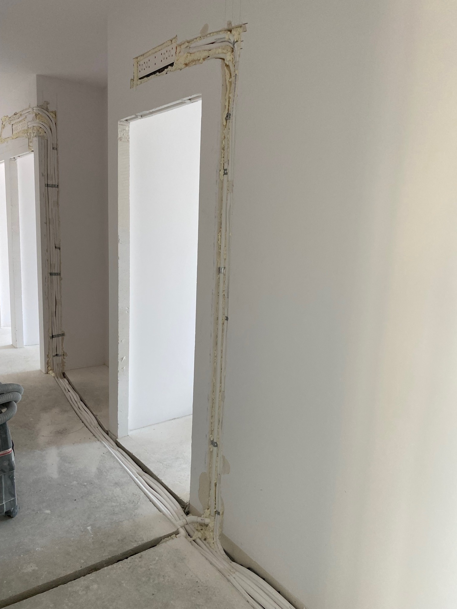 Montaż instalacji elektrycznej w nowym budynku, widoczne kable prowadzone wzdłuż ścian i nad ościeżnicami, zabezpieczone pianką montażową, surowy beton na podłodze.