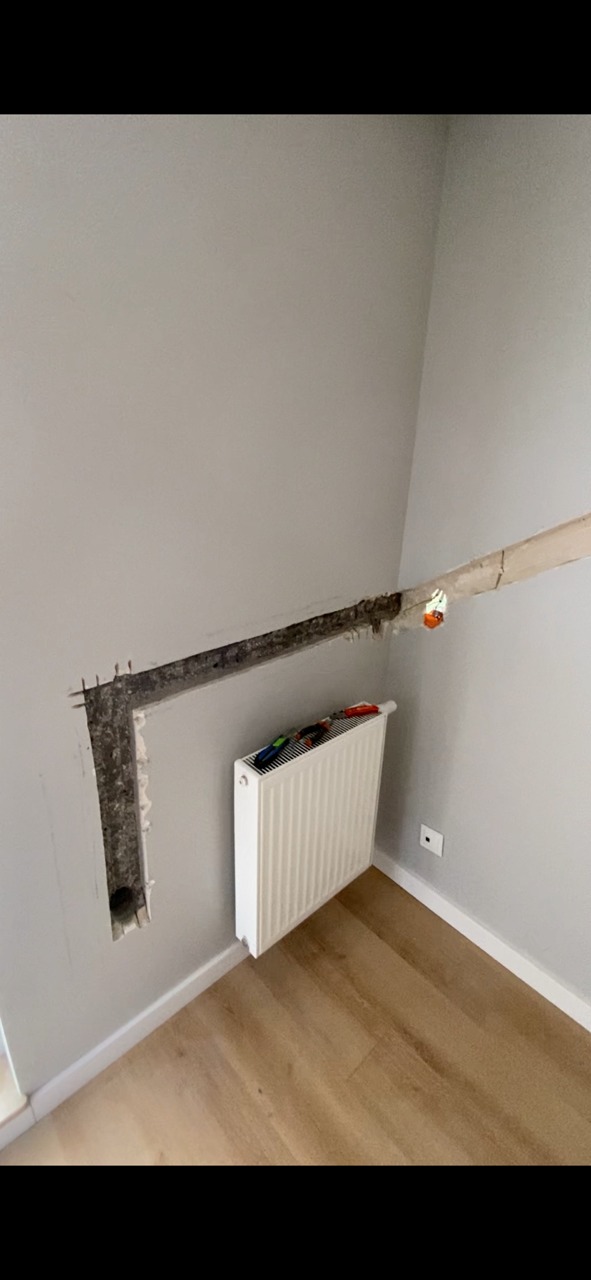 Przygotowanie pod instalację klimatyzacji w domu: wycięty kanał w ścianie, obok grzejnik i narzędzia.