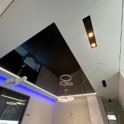 Nowoczesny salon z czarnym lustrzanym sufitem, oświetleniem LED w kolorze niebieskim i białym oraz wiszącymi okrągłymi lampami.