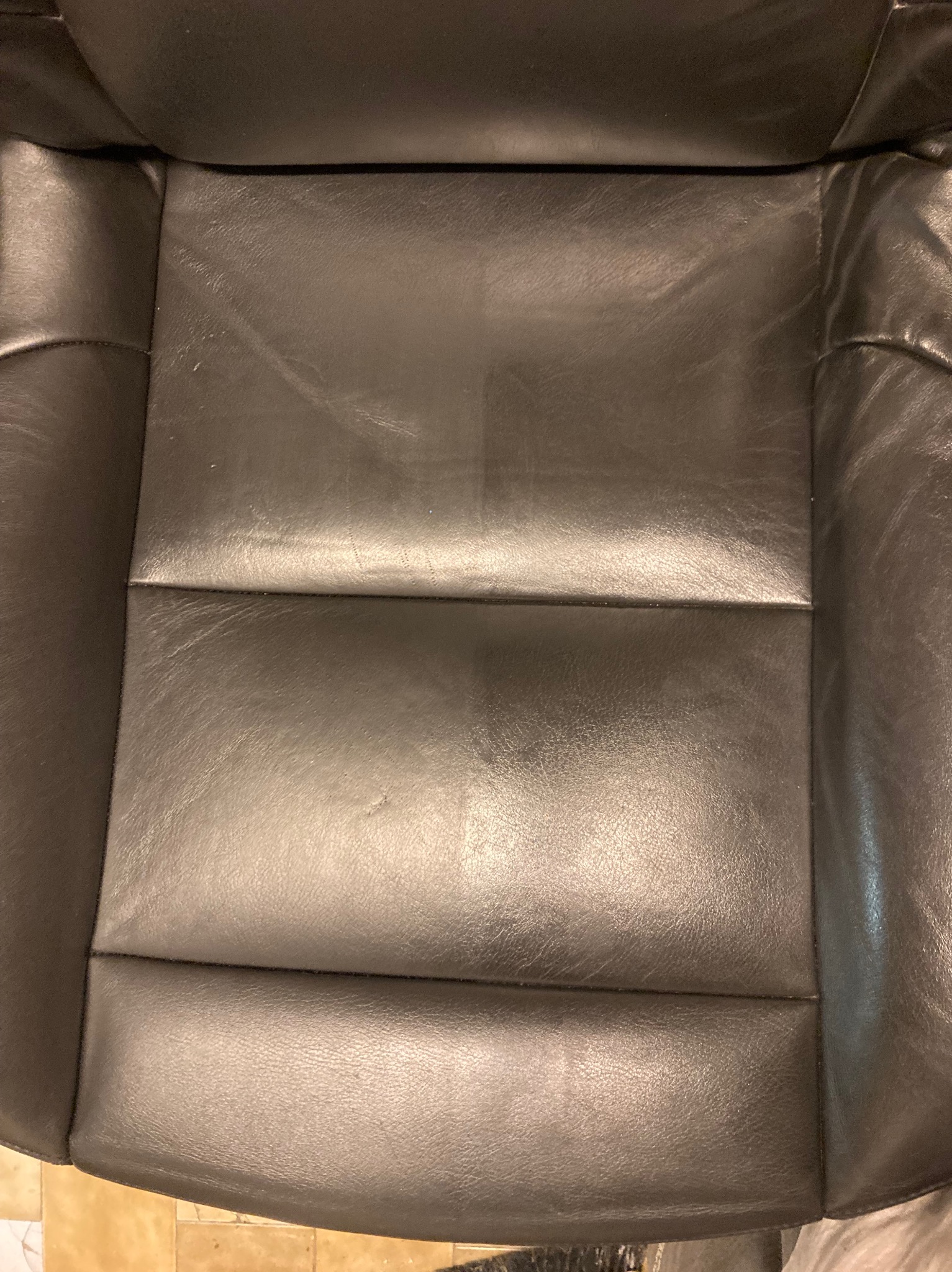 Zbliżenie na czarne skórzane siedzenie samochodowe z widocznymi śladami użytkowania i delikatnymi zarysowaniami na powierzchni.