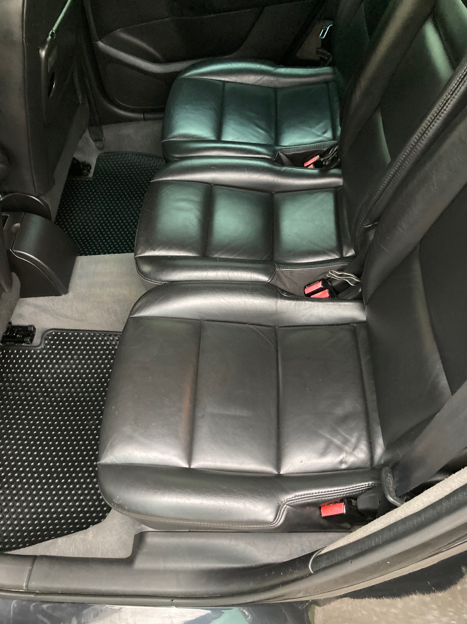 Wnętrze samochodu z widocznymi czarnymi, skórzanymi tylnymi siedzeniami i gumowymi dywanikami z wypustkami.