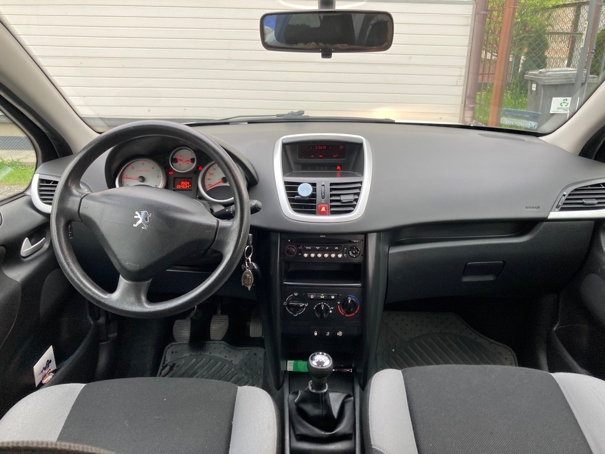 Wnętrze samochodu marki Peugeot sfotografowane w Kielcach, z widoczną deską rozdzielczą, kierownicą i siedzeniami z szaro-czarną tapicerką. Na przedniej szybie odbija się budynek.