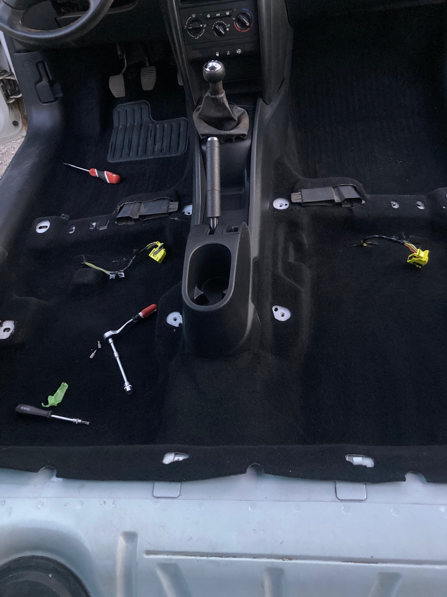 Wnętrze samochodu w trakcie demontażu, widoczne narzędzia i częściowo zdjęta tapicerka podłogowa, przygotowanie do czyszczenia.