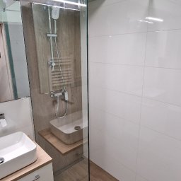 Marktor Marcin Poznański - Nowoczesna łazienka z kabiną prysznicową typu walk-in, umywalką nablatową i drewnopodobnymi płytkami na podłodze oraz ścianie w strefie prysznica.