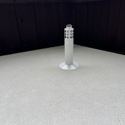 SDV GROUP - Biały kominek wentylacyjny z perforacją, zamontowany na jasnym, teksturowanym dachu, z widoczną brązową deską okapową w tle.