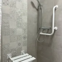 Nowoczesna kabina prysznicowa z siedziskiem dla osób z ograniczoną mobilnością i uchwytem, wykończona szarymi płytkami z dekoracyjnym wzorem.