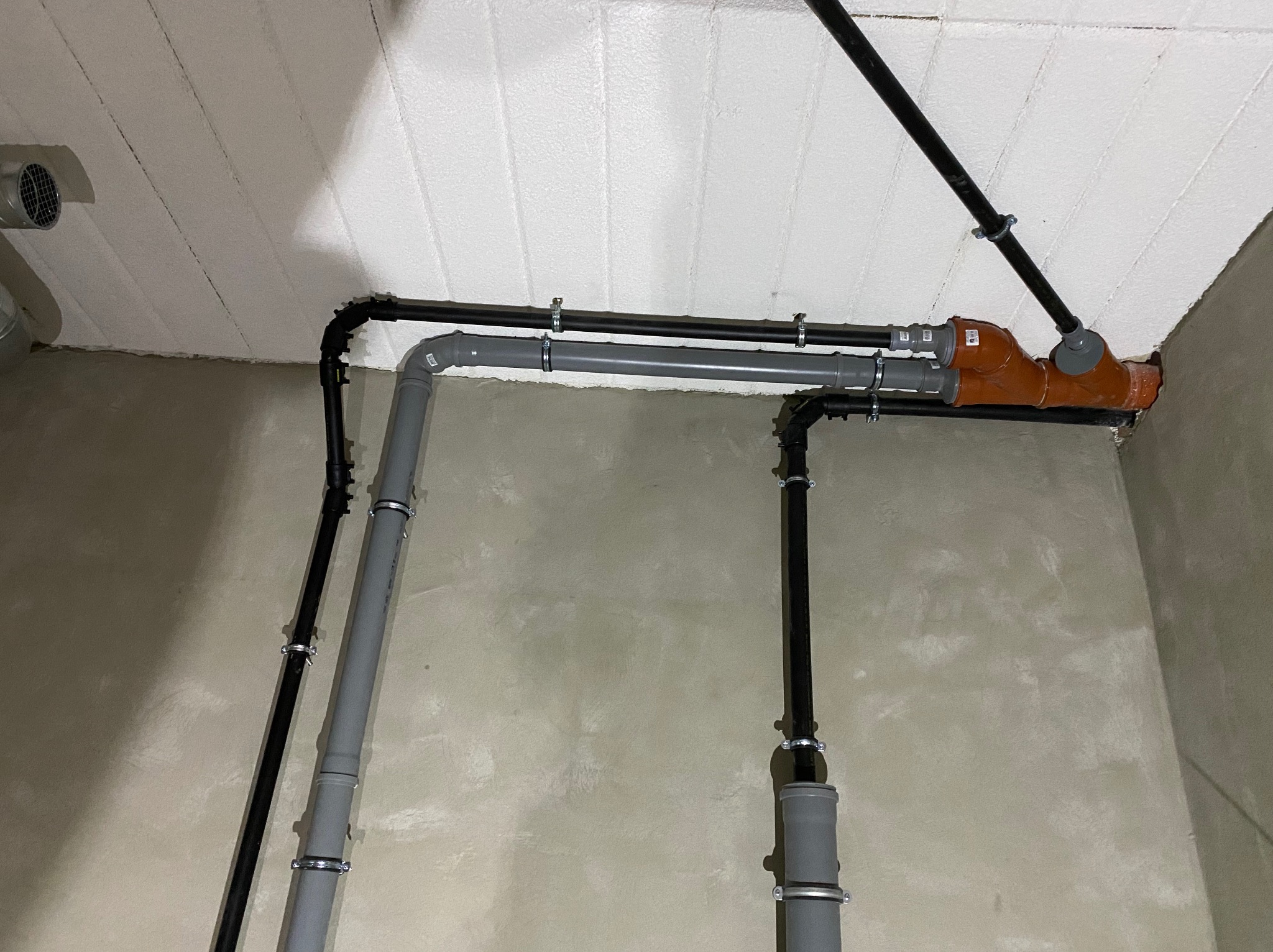 Szare i czarne rury instalacji wodnej i kanalizacyjnej zamocowane do sufitu i ściany w surowym stanie.