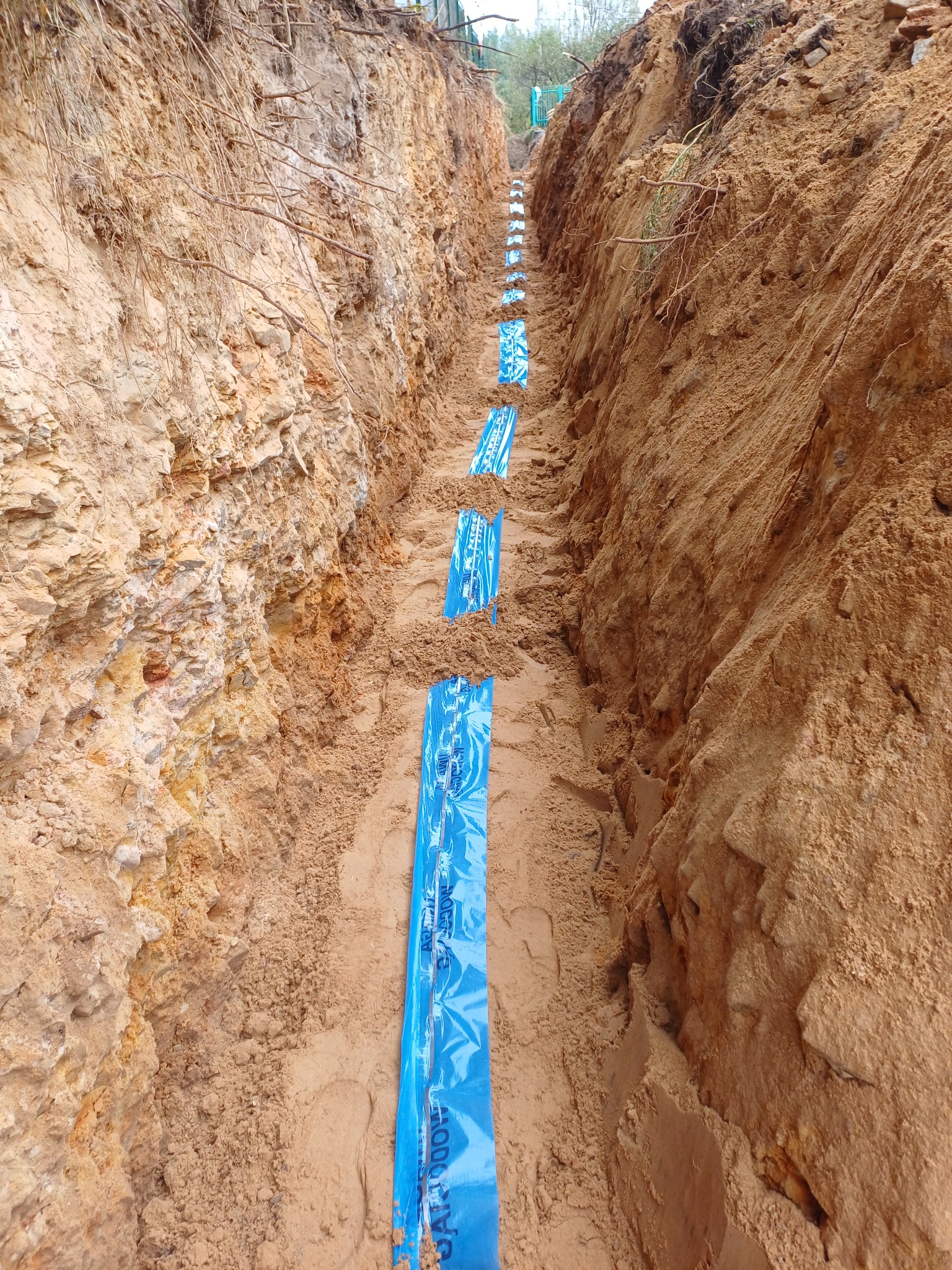 Wykop w ziemi z ułożoną, niebieską folią ochronną na dnie, zabezpieczającą rury instalacji.