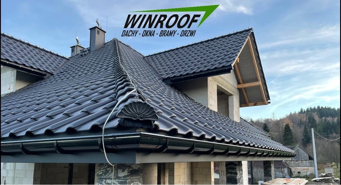 Nowy dom w trakcie budowy z ciemną dachówką ceramiczną i systemem rynnowym, widoczny logo firmy WINROOF na górze zdjęcia.