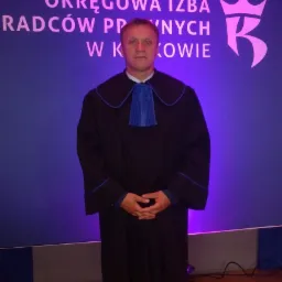 Portret mężczyzny w todze prawniczej na tle logo Okręgowej Izby Radców Prawnych w Krakowie.