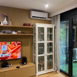 InstalTeam - Biała klimatyzacja Hyundai zamontowana nad witryną w salonie. Widoczny wyświetlacz 17 stopni. Nowoczesne wnętrze z drewnianą boazerią i dużym oknem balkonowym.