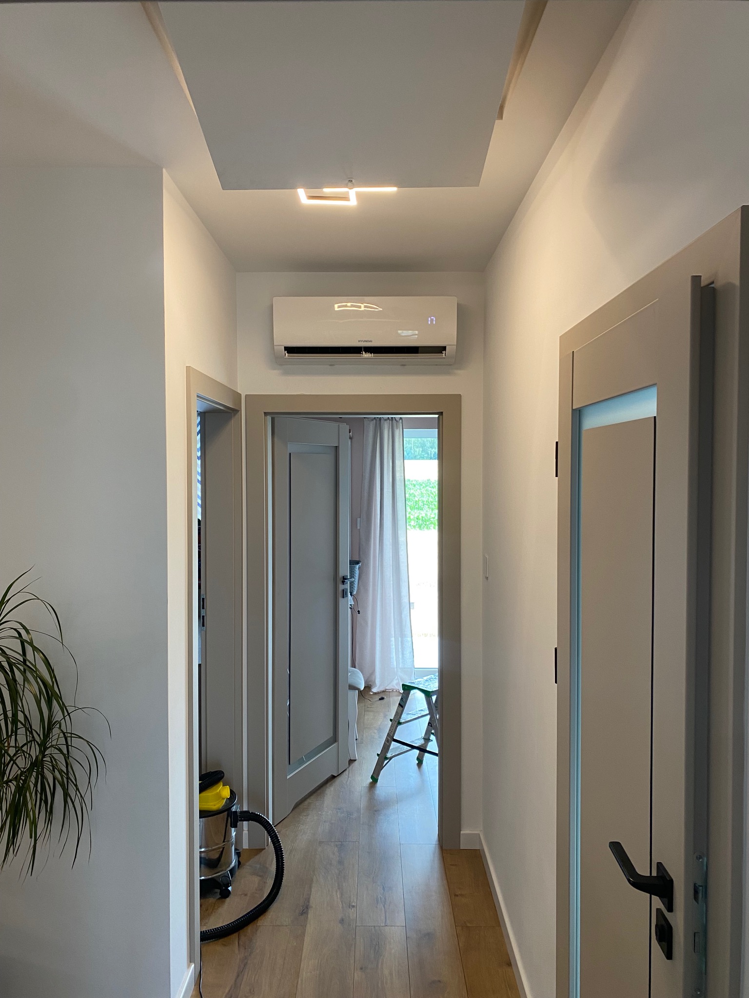 Klimatyzator Hyundai zamontowany nad drzwiami w korytarzu domu w Stróży. Widoczny fragment schodów i odkurzacza.