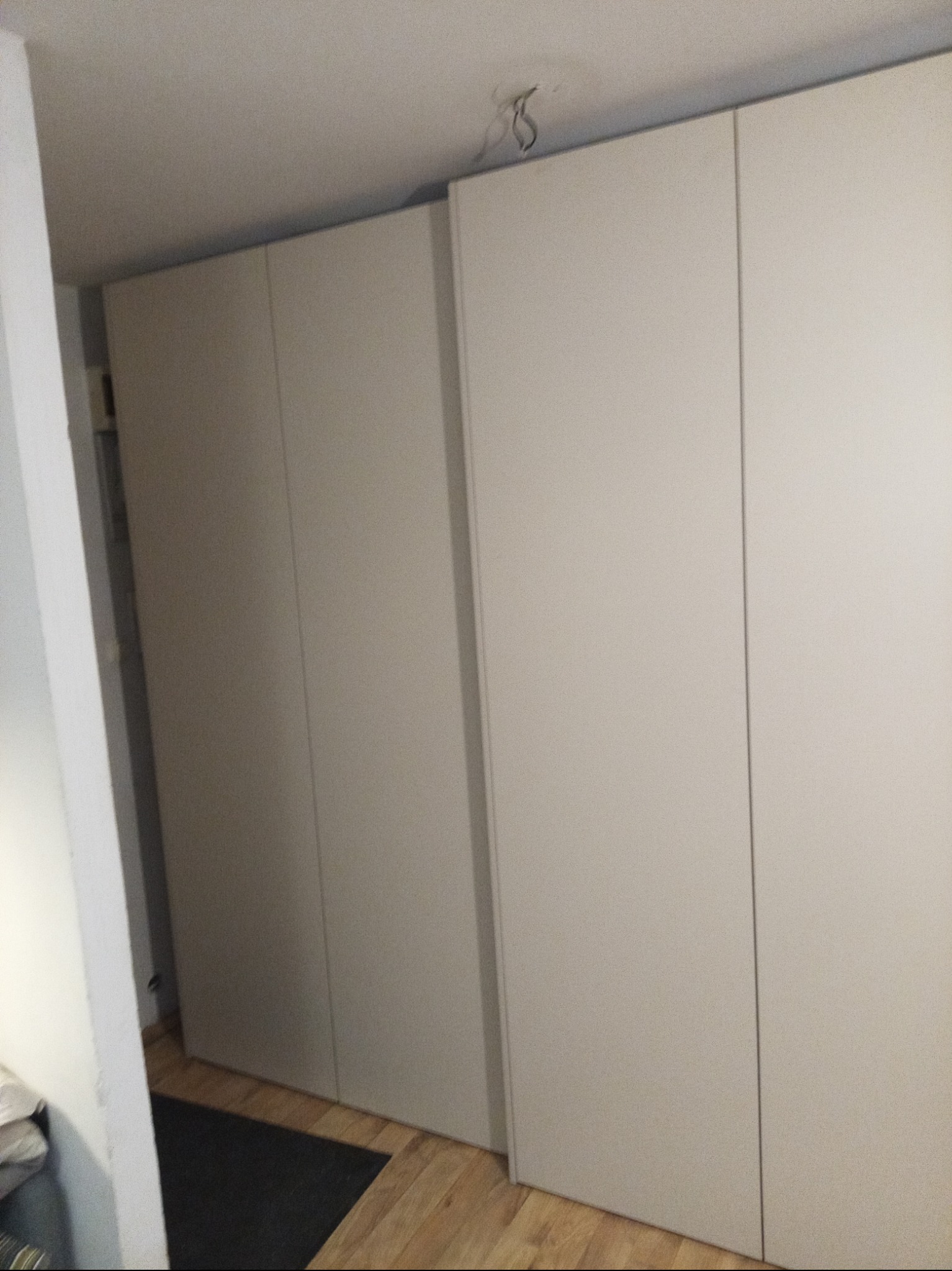 Czterodrzwiowa, jasna szafa wnękowa z widocznymi kablami wystającymi z sufitu i fragmentem podłogi z paneli.