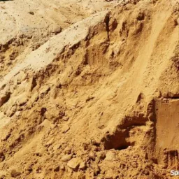 Duża pryzma piasku w odcieniach beżu i brązu, z widoczną strukturą ziarnistą i nierówną powierzchnią.