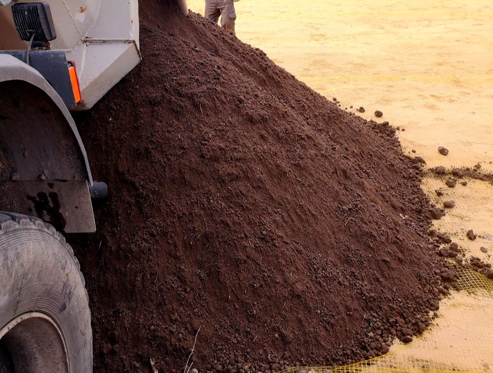 Wyładunek ciemnej, wilgotnej ziemi z ciężarówki w Starachowicach, widoczny fragment koła i żółta siatka pod spodem.