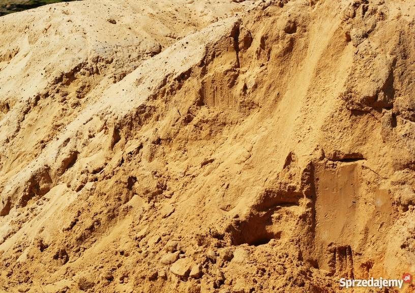 Duża pryzma piasku w odcieniach beżu i brązu, z widoczną strukturą ziarnistą i nierówną powierzchnią.