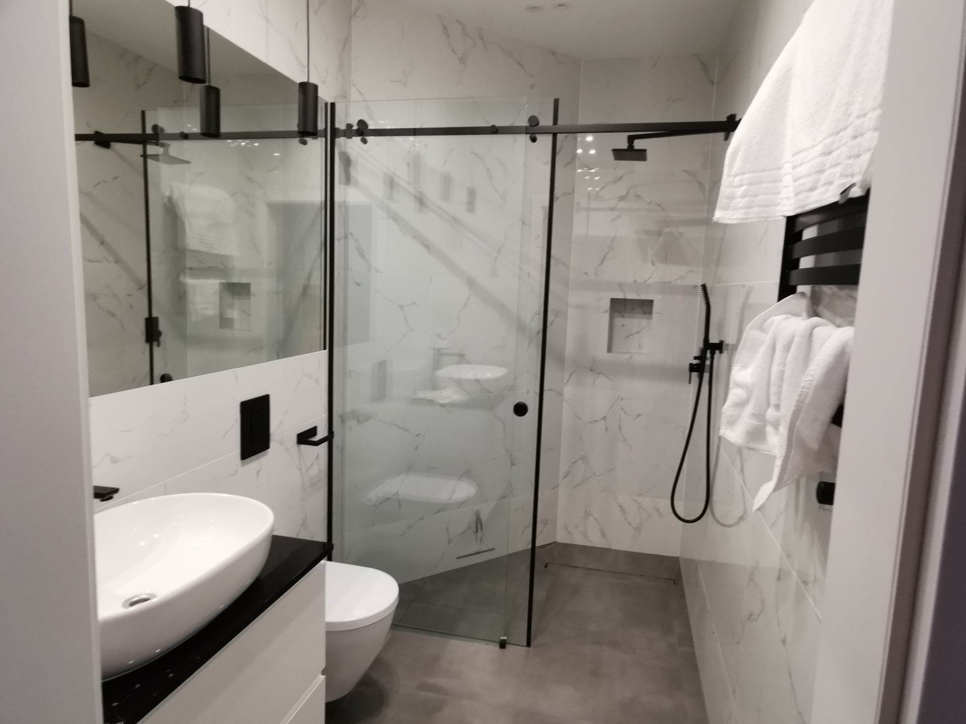 Nowoczesna łazienka z kabiną prysznicową typu walk-in z czarnymi detalami, marmurowymi płytkami na ścianach i wiszącą umywalką.