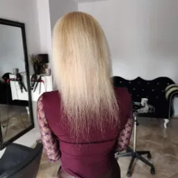 Blond włosy klientki przed zabiegiem, widok z tyłu, na tle salonu z czarną sofą i lustrem.