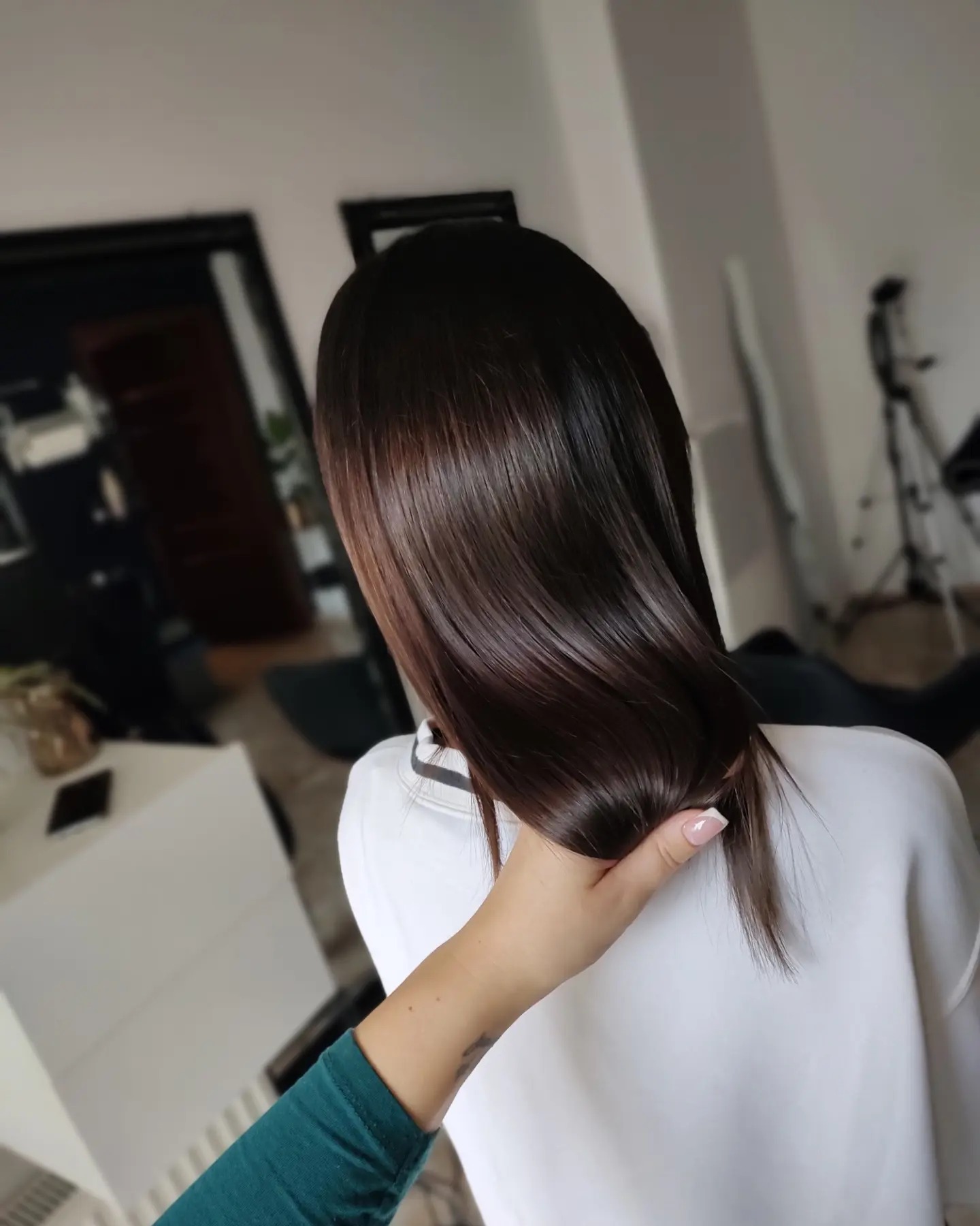 Błyszczące, ciemne włosy kobiety po zabiegu, trzymane w dłoni z delikatnym manicure, widok z tyłu.