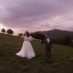 Para młoda trzymająca się za ręce na łące o zmierzchu, góry w tle.