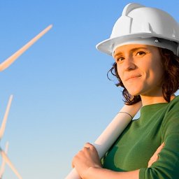 POLSUN Energy Sp. z o.o. - Kobieta w kasku trzymająca zwój planów na tle turbin wiatrowych i błękitnego nieba.