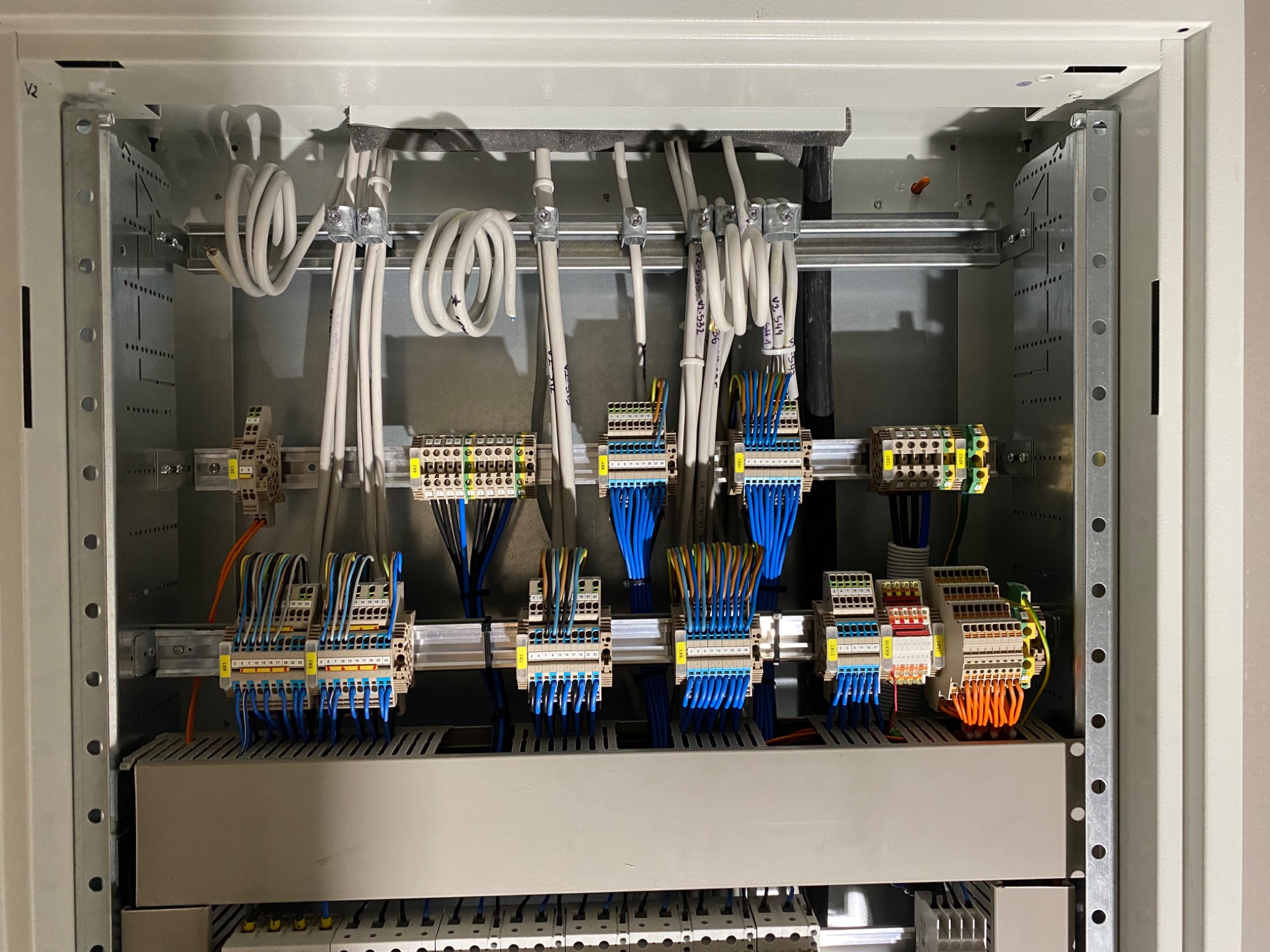 Wnętrze szafy sterowniczej z widocznymi przewodami, złączkami i listwami zaciskowymi, uporządkowane kable w peszlach, metalowa konstrukcja szafy z perforacją.